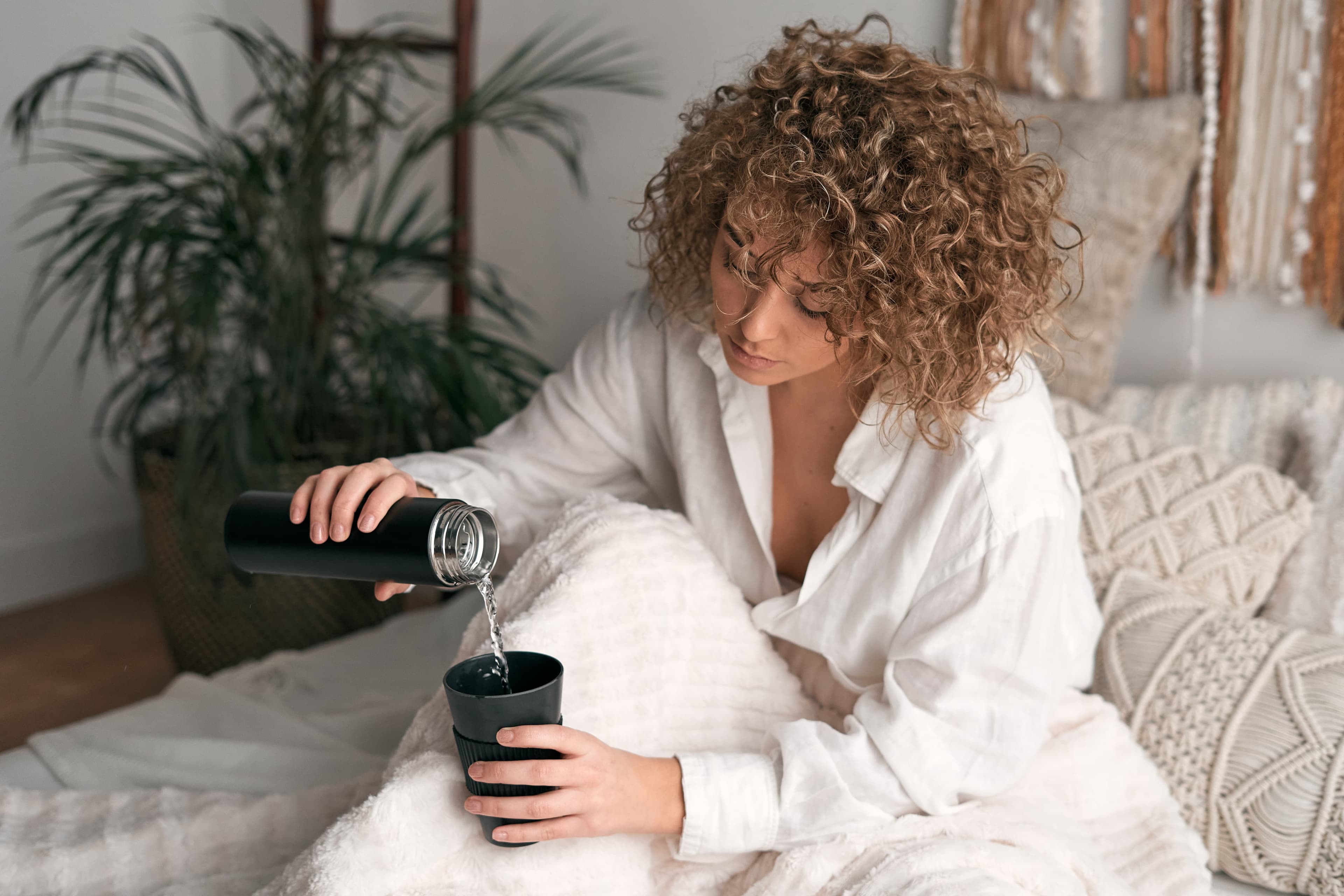 A woman pouring herself water sitting on her Leesa bed