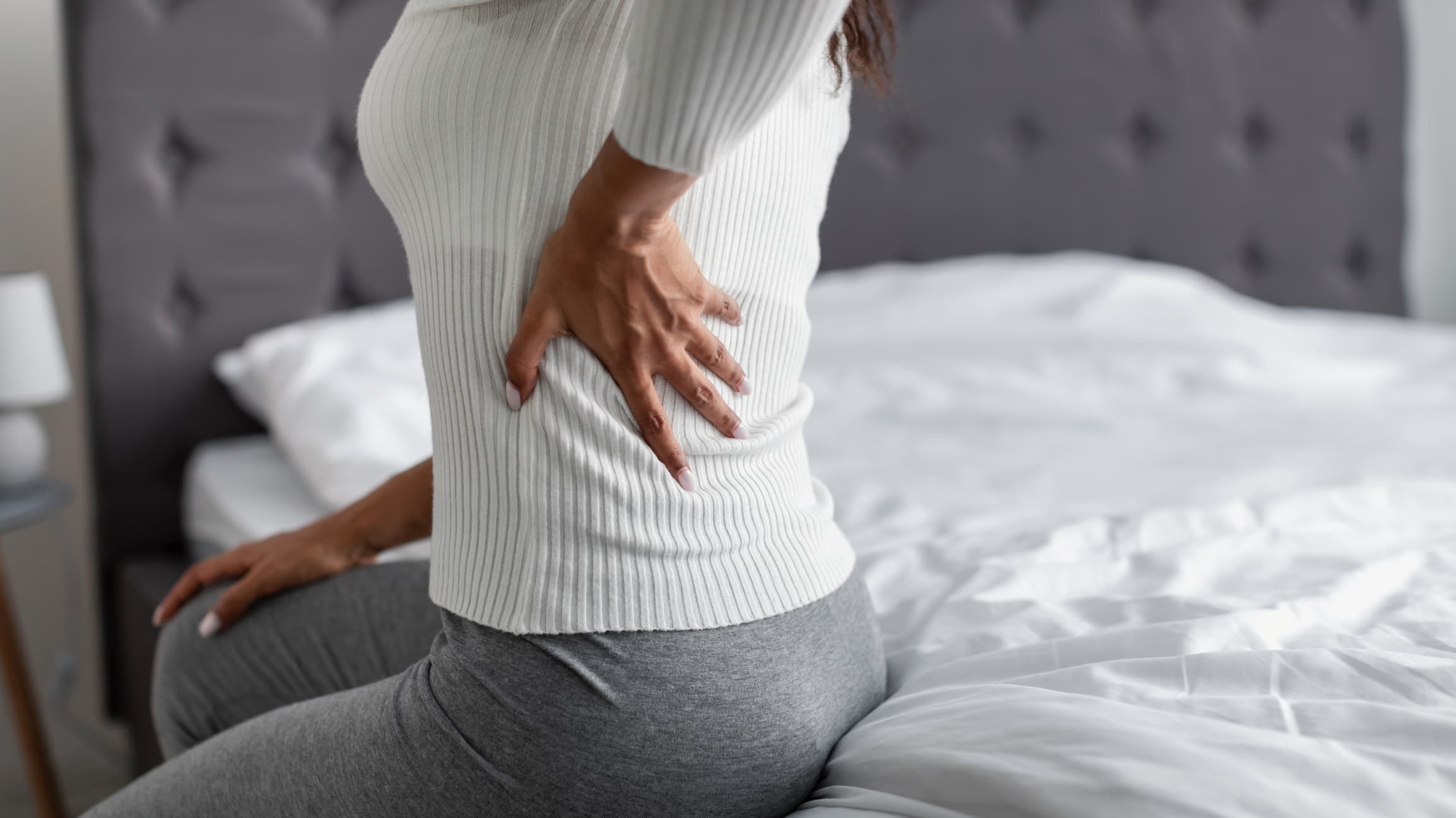 A woman sitting on her Leesa mattress in pain