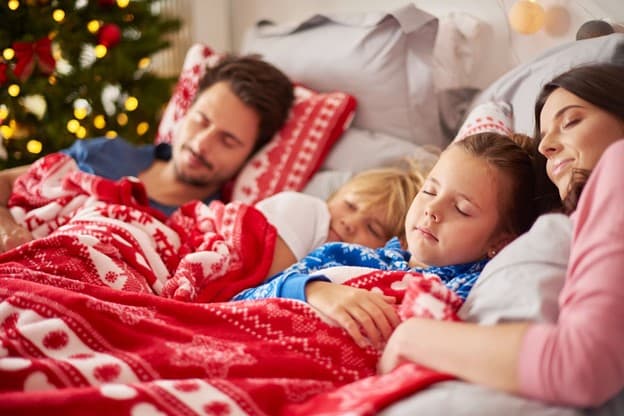 A family lying in a bed in a festive red blanket and pillow